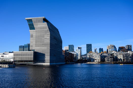 Stunning view of the contemporary Munch Museum and Oslo skyline reflected on the waterfront under a clear blue sky.