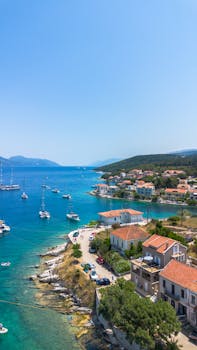 Scenic aerial shot of a charming coastal village with stunning turquoise waters and anchored sailboats on a sunny day.