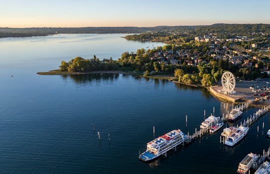 A scenic aerial photo of Lake Maggiore with ferris wheel and boats at sunset, capturing serene waters and lush landscape.